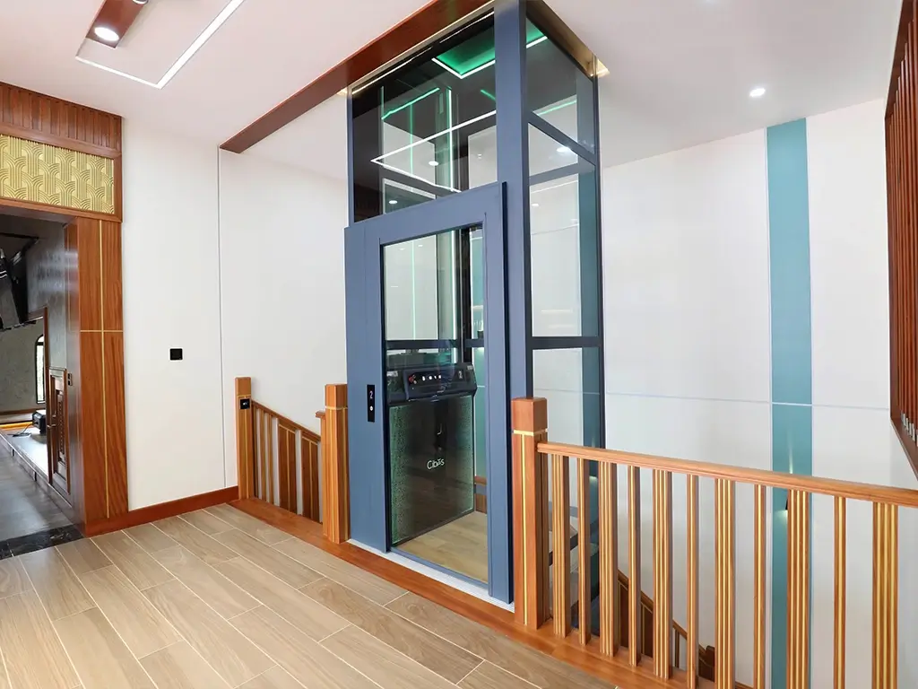 Cibes Voyager platform lift with glass shaft and blue-grey door, installed next to wooden handrails in a modern home interior.