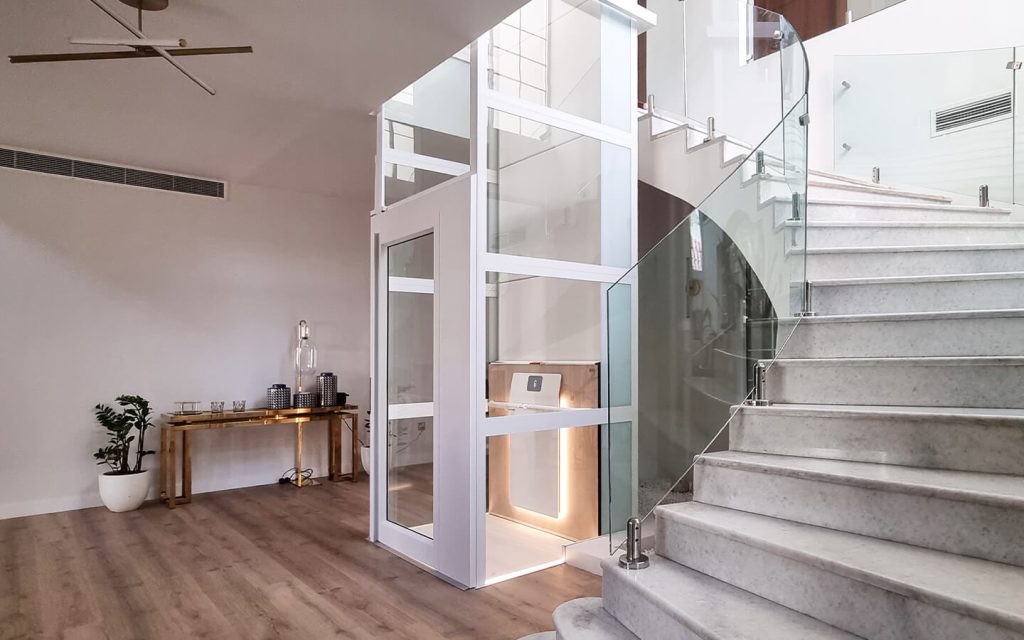 Cibes Air home elevator with white panoramic shaft installed beside a marble staircase in a premium villa in Mirdif, Dubai.