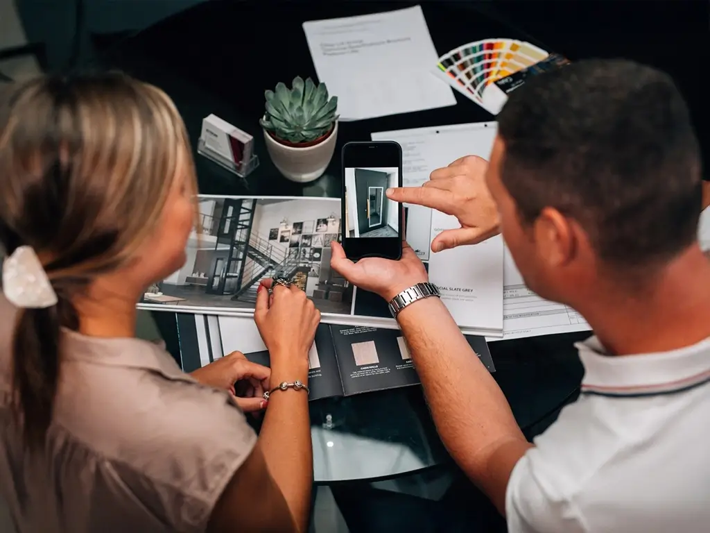 Two people reviewing home lift design options on a smartphone and printed catalog during a consultation.