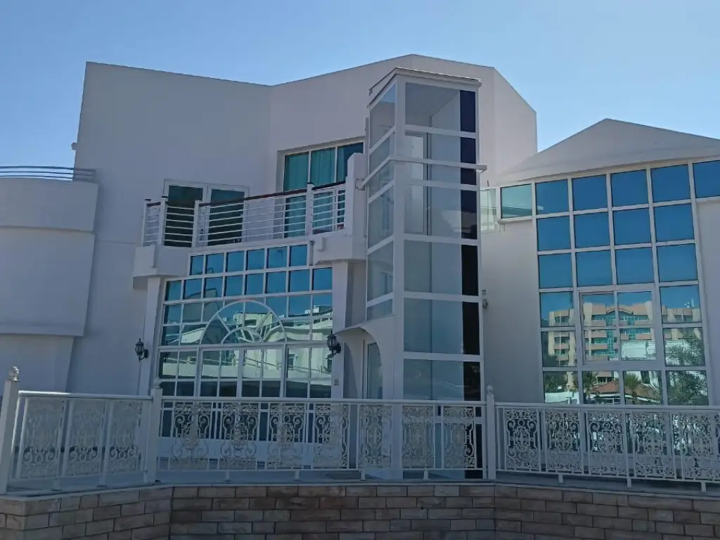 Outdoor home elevator installation in Mankhool Dubai with external glass shaft attached to a white villa façade.