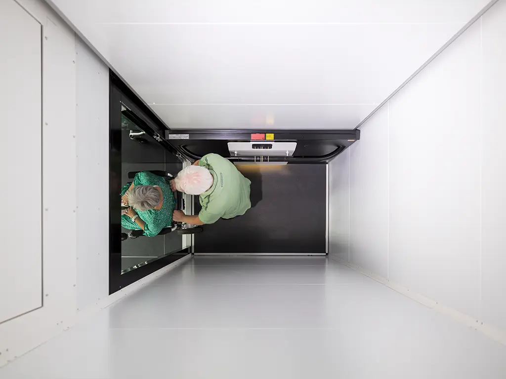 Elderly couple using home lift inside a residential elevator cabin.